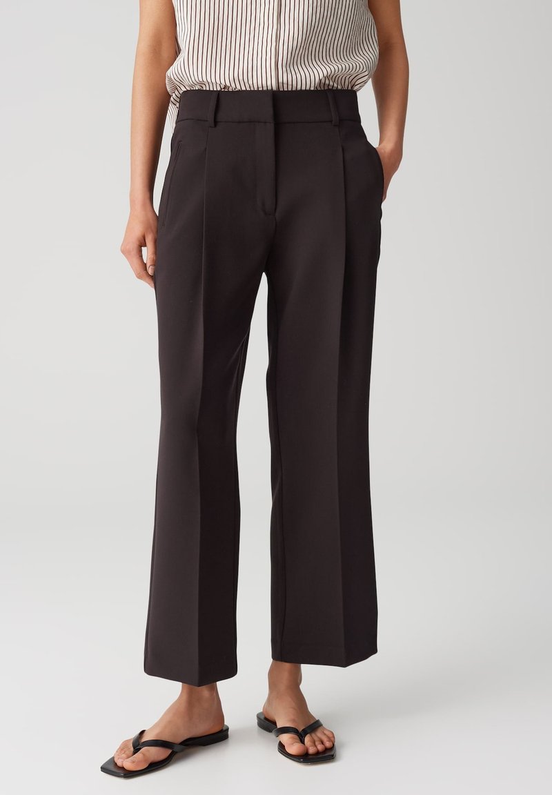 High-waisted black wide-leg trousers made of smooth fabric, featuring sharp creases, side pockets, and a tailored fit.