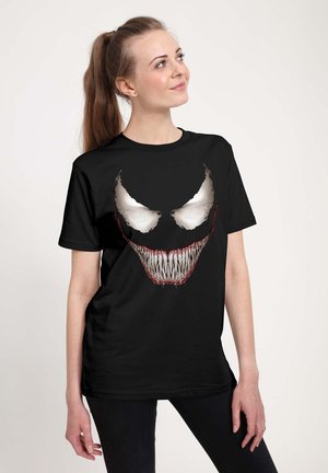 T-shirt en coton noir avec un grand design graphique représentant un visage de monstre blanc et rouge avec des dents acérées et des traits exagérés.