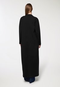Lungo cappotto nero con una vestibilità rilassata, dotato di maniche lunghe e taglio dritto, realizzato in un tessuto morbido e texturizzato.