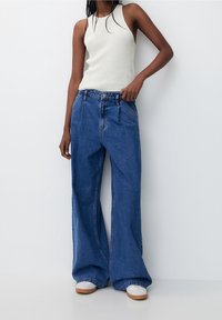 Breda blå denimjeans med hög midja, med framfickor och en urtvättad look. Matchas med en figurnära vit ribbad linne.