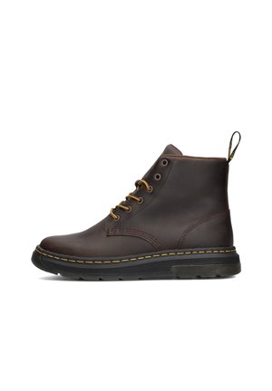 Dunkelbrauner Leder-Stiefelette mit gelber Nahtverzierung, schwarzer Gummisohle, Schnürfront und Lasche an der Ferse vor weißem Hintergrund.