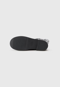 Semelle en caoutchouc noir avec des rainures horizontales pour une meilleure traction. Conçu pour la durabilité. Présente un branding minimal sur le côté.