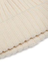 Crèmekleurige ribbelgebreide stof opgevouwen om de textuur en de stikseldetails aan de rand van een zacht, warm kledingstuk te tonen.