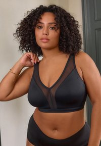 Zwarte bralette met een transparante mesh inzet, voorzien van een V-hals ontwerp, brede bandjes en een gladde textuur, gecombineerd met bijpassende hoge taille broekjes.