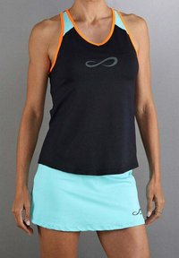 Mujer vistiendo una camiseta sin mangas negra y naranja con una falda azul claro, ambos con un pequeño logo de símbolo infinito.