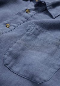 Tummansininen pellavapaita, jossa on napitettava etuosa, erottuva rakenne ja vasemmalla puolella näkyvillä ompeluaksoilla varustettu päällyspocketti.