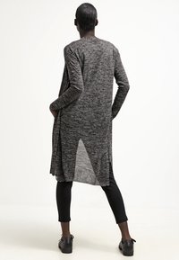 Largo cárdigan negro y gris hecho de tela de punto texturizada, con un dobladillo recto, aberturas laterales y un corte relajado, combinado con leggins negros.