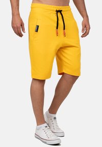 Geel elastische tailleband shorts met zwarte trekkoord, zijzak en een rechte snit, gedragen met witte sneakers.