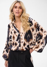 Silk blouse with a bold animal print in beige, black, and brown. Features a button-front, long sleeves, and relaxed fit.