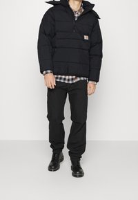 Svart dunjacka med en dragkedjeförsedd frontal ficka, kombinerad med en rutmönstrad skjorta och svarta cargobyxor, bärs med svarta snörstövlar.