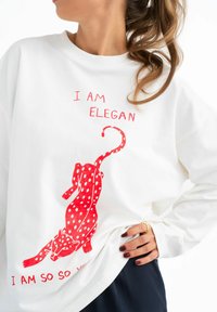 Witte sweatshirt met een rode gestippelde luipaardafbeelding en de tekst "IK BEN ELEGANT" en "IK BEN ZO JIJ" in het rood. Zacht katoen, ontspannen pasvorm.