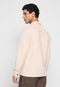 Beige shirt met structuur, een kraag, lange mouwen en een slanke pasvorm. Voorzien van een enkele achterpas en manchetten met knopen.