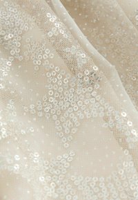 Tissu beige transparent orné de sequins circulaires et de petits détails brillants, créant un effet texturé et superposé avec des motifs d'étoiles.