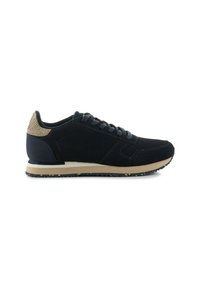 Black athletic shoe made of mesh and suede, features a textured beige heel, gray laces, and a beige midsole with a patterned outsole.