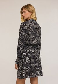 Abito nero a maniche lunghe con un motivo geometrico bianco e vita stretta. Tessuto morbido, gonna alla lunghezza del ginocchio, polsi con bottoni e colletto da camicia.