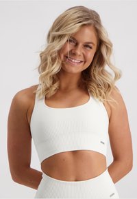 White ribbed sports bra with a square neckline and cut-out sides. Features a subtle logo accent on the band. Smooth, stretchy material.