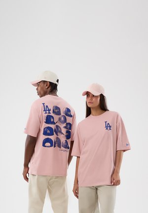 Due modelle che indossano t-shirt e cappellini rosa dei LA Dodgers, una mostra il logo sul davanti, l'altra mostra diversi design di cappellini blu sul retro.