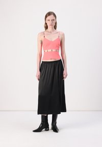 Coral crop top with thin straps and decorative hardware paired with a long black satin skirt and pointed black heeled boots.