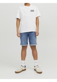 Camiseta blanca de manga corta con el texto "Malibu", pantalones cortos de mezclilla azules con dobladillos enrollados, zapatillas blancas y beige, y calcetines blancos con un patrón.