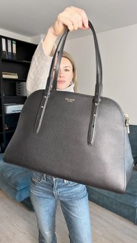 Μαύρη δερμάτινη τσάντα χειρός με δομημένο σχήμα, διπλές λαβές στην κορυφή, χρυσές λεπτομέρειες και ορατά ραφές. Υφή επιφάνειας.