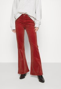 Pantalons en velours côtelé rouge évasés avec une finition texturée, associés à un sweat-shirt gris clair. Des bottes à talons noires complètent la tenue.