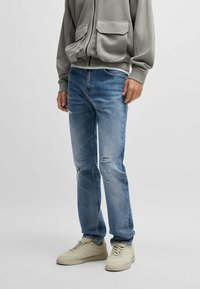 Ljusblå denimjeans med rak passform, prydda med slitna knädetaljer, tillsammans med krämfärgade sneakers och en grå hoodie.