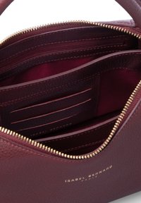 Intérieur d'un sac à main en cuir bordeaux avec une fermeture éclair dorée, comprenant des emplacements pour cartes, une poche zippée et une texture lisse. Logo imprimé en or.