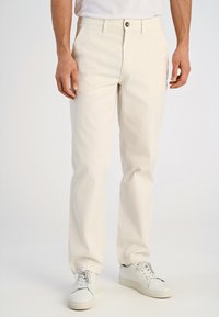 Chinos beige chiaro in cotone con taglio dritto, dotati di chiusura con un solo bottone e tasche laterali, abbinati a sneakers bianche.