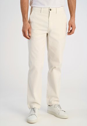 Lichtbeige chinos van katoen met een rechte snit, voorzien van een enkele knoopsluiting en zijzakken, gecombineerd met witte sneakers.