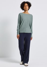 Maglione a maglia verde chiaro con scollatura a barca, maniche lunghe, abbinato a pantaloni blu navy larghi e sneakers bianche.