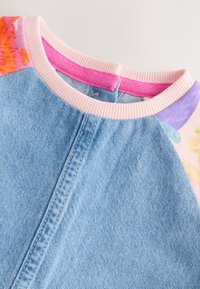 Denim overhemd met roze geribbelde kraag en kleurrijke bloemenmouwen. Heeft een zachte textuur en contraststiksels langs het voorpand.