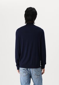 Jersey de cuello alto de color navy, tejido de punto, manga larga, diseño simple, combinado con unos vaqueros de color azul claro con bolsillos traseros curvados.