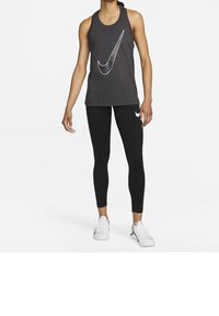 Schwarzes sportliches Tanktop mit einem großen weißen Nike-Swoosh-Logo, kombiniert mit schwarzen Leggings und weißen Turnschuhen, geeignet für Workouts.