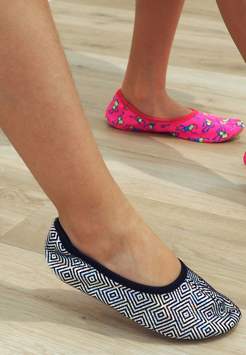Zwart-witte platte schoenen met geometrische patronen aan de ene voet, en roze schoenen met bloemdessin aan de andere voet, beide op een houten vloer.