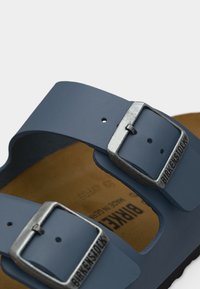 Μπλε σανδάλι Birkenstock με δύο ρυθμιζόμενες ασημένιες αγκράφες και ορατή καφέ βάση παπουτσιού.