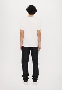 White short-sleeve t-shirt paired with dark denim jeans. The jeans are straight-cut with a classic five-pocket design. White sneakers complete the outfit.