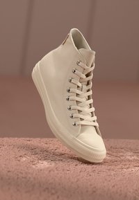 High-top sneakers made of cream-colored leather, featuring metallic eyelets, matching laces, and a textured rubber sole.