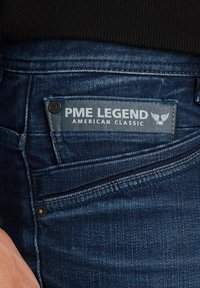 Jeans de mezclilla azul oscuro con una etiqueta visible que dice "PME LEGEND AMERICAN CLASSIC." Presenta costuras decorativas y un bolsillo frontal.