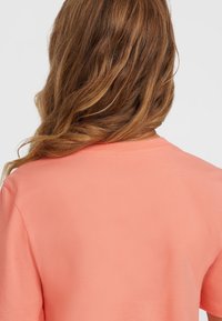 Camiseta de manga corta y cuello redondo en algodón coral con una textura suave, con un respaldo liso y costuras discretas a lo largo del cuello.