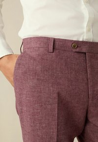 Bordeauxfarbene Hose aus strukturiertem Stoff. Mit einem Knopfverschluss, seitlichen Taschen und einem lässigen Schnitt.