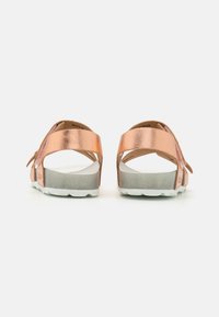 Roze gouden sandalen met een gestructureerde metallic bovenkant, verstelbare strap, witte voetbed en grijze, enigszins verhoogde zool, gezien vanuit de achterkant.