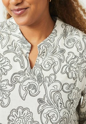 Tessuto bianco con ricami neri a paisley presenta un collo a V e una finitura morbida e textured. I dettagli floreali sono molto evidenti.