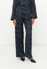 Navy patterned wide-leg pants with a geometric design. Made from a textured fabric, featuring a high waist and side pockets, paired with heels.