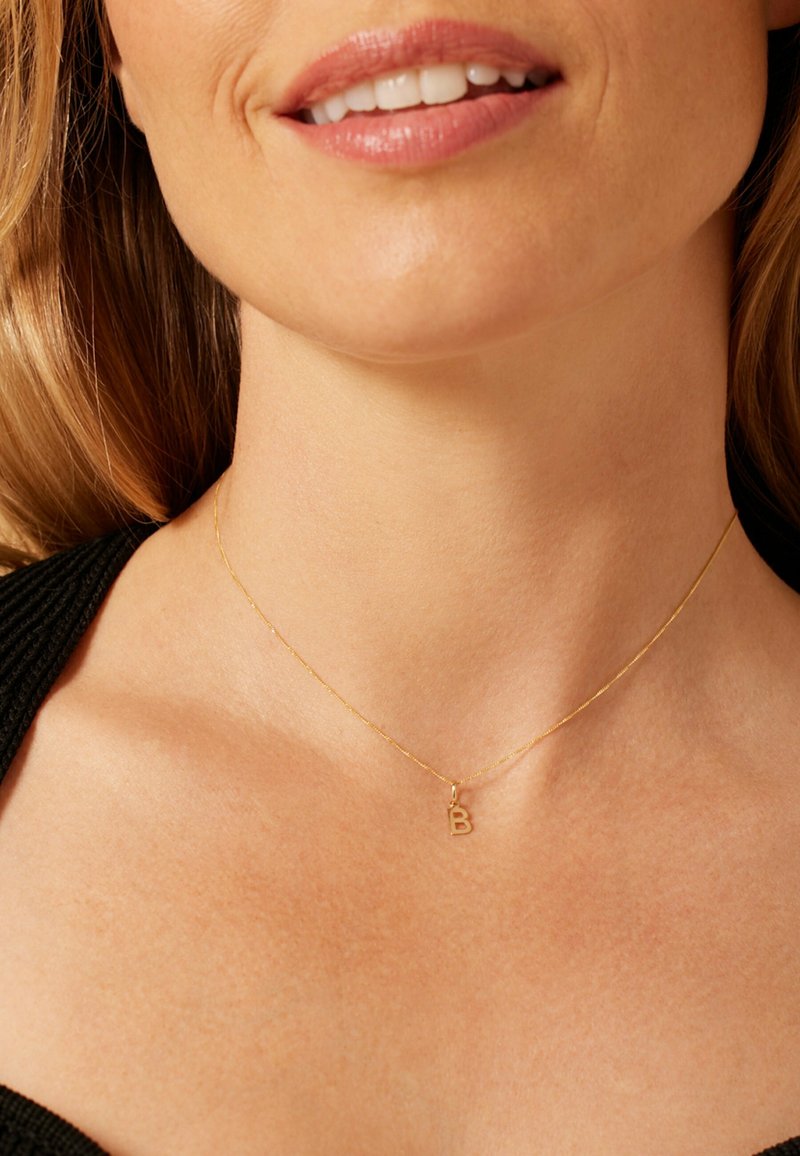 Gouden ketting met een fijn kettinkje en een kleine, hoofdletter "B" hanger. Gladde oppervlakte, minimalistisch ontwerp, geschikt voor dagelijks gebruik.