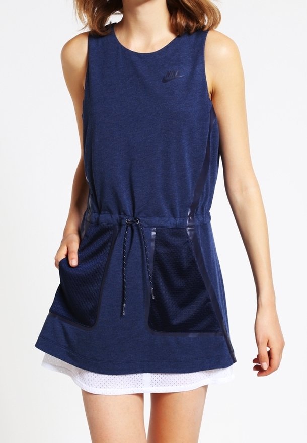 Sleeveless navy blue Nike dress with front drawstring waist and two large mesh pockets, worn over a white skirt.