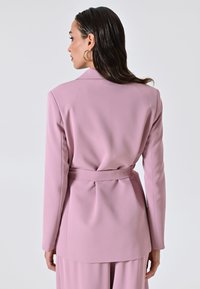 Rosa Blazer mit taillierter Passform, langen Ärmeln, ausgeprägten Revers, Details mit Gürtel in der Taille und glatter Stofftextur. Rückansicht gezeigt.