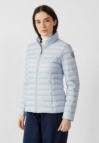 Chaqueta acolchada azul claro, con diseño acolchado de líneas verticales, cuello alto, cremallera completa, bolsillos laterales y un logo en la manga izquierda.