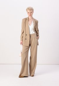 Beige skreddersydd blazer med svarte knapper, matchende vide bukser, hvit topp og en liten rosa veske. Glatt stoff, strukturert passform.