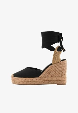 Espadrilă cu talpă din canvas negru, cu o talpă din jute împletit texturat și curele pentru gleznă. Prezintă un vârf rotunjit și un accent pe toc cu un model.