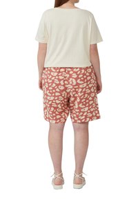 Crème top met korte mouwen gecombineerd met koralen shorts met een witte stippenpatroon. Model draagt lichtgekleurde sleehak-sandalen.